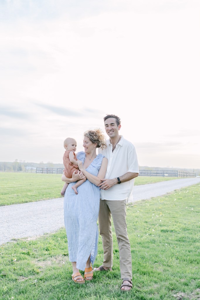 family of three poses in green field, mother holds young son 