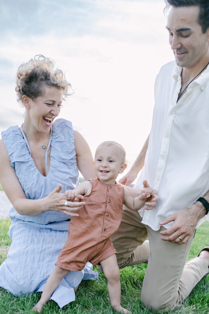 mother holds child's hands as he takes a step, dad with them