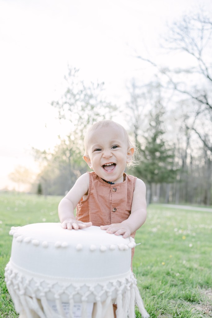 young boy poses by chair in green field 