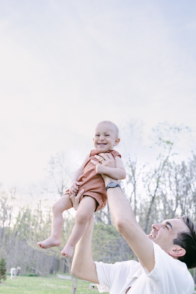 father holds up young smiling son 