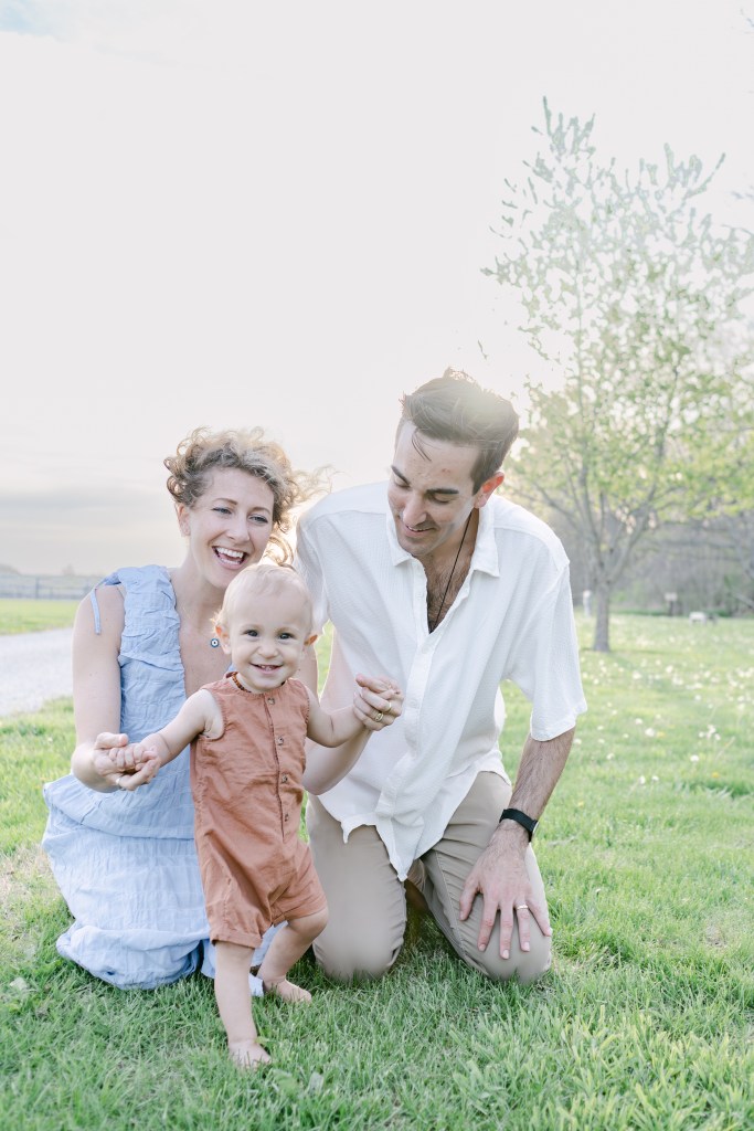 family of three poses in green feild, son starts to walk 