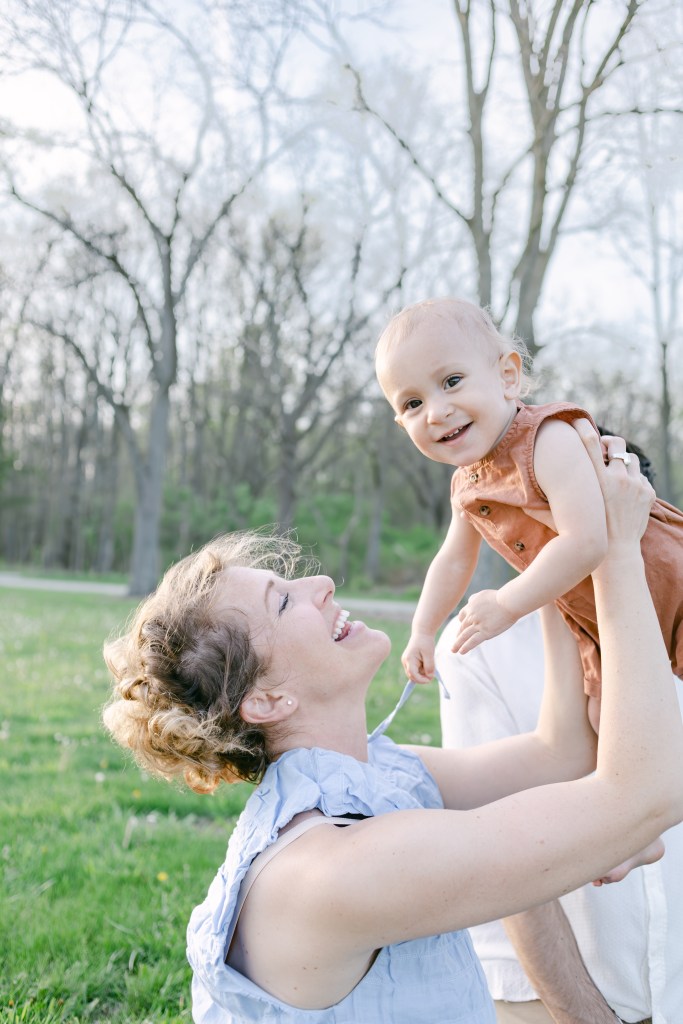 mother holds young son up in air, smiles at him 